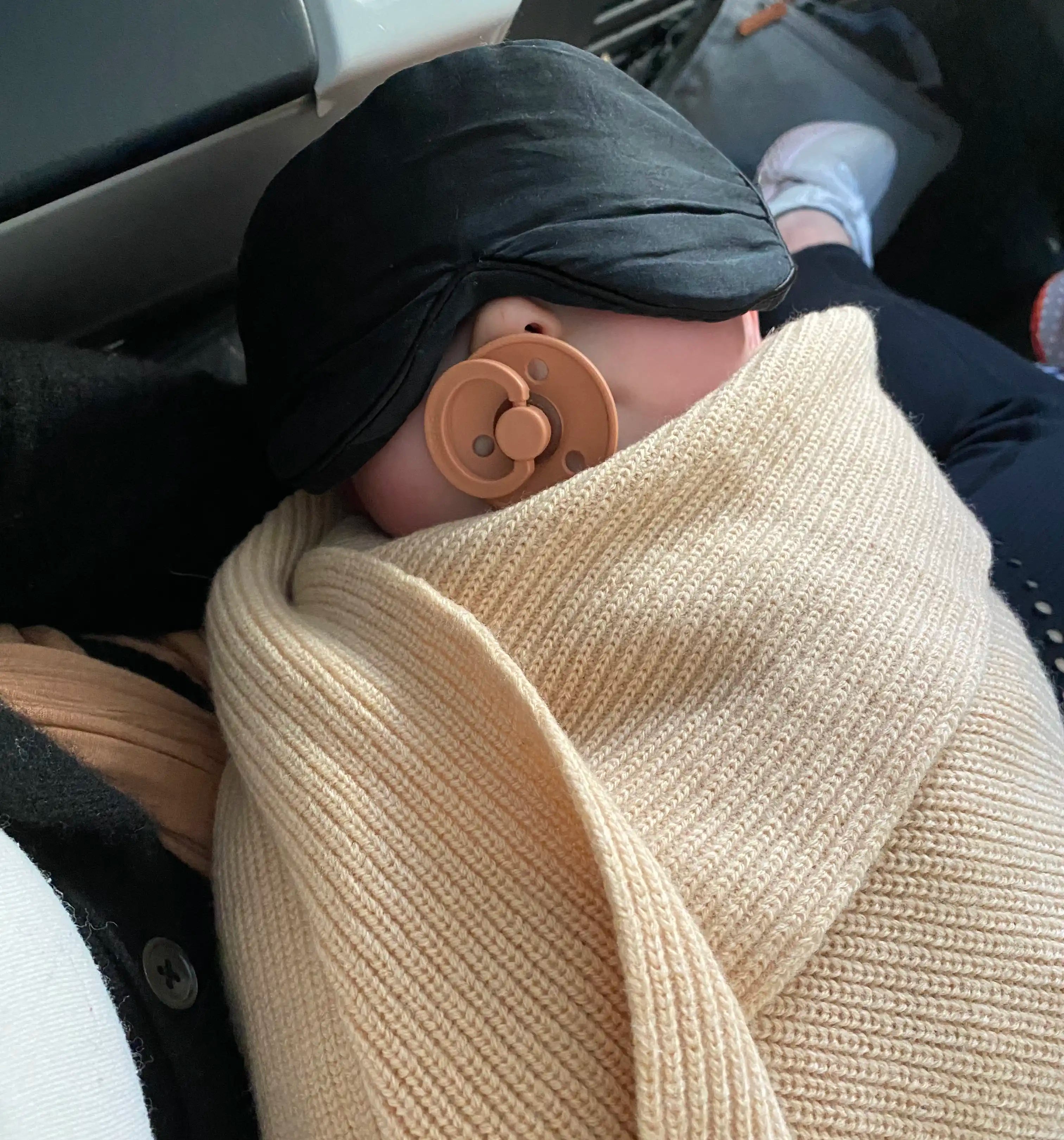 Baby wrapped in beige merino AU Baby blanket. Travel tips for babies on airplaines.