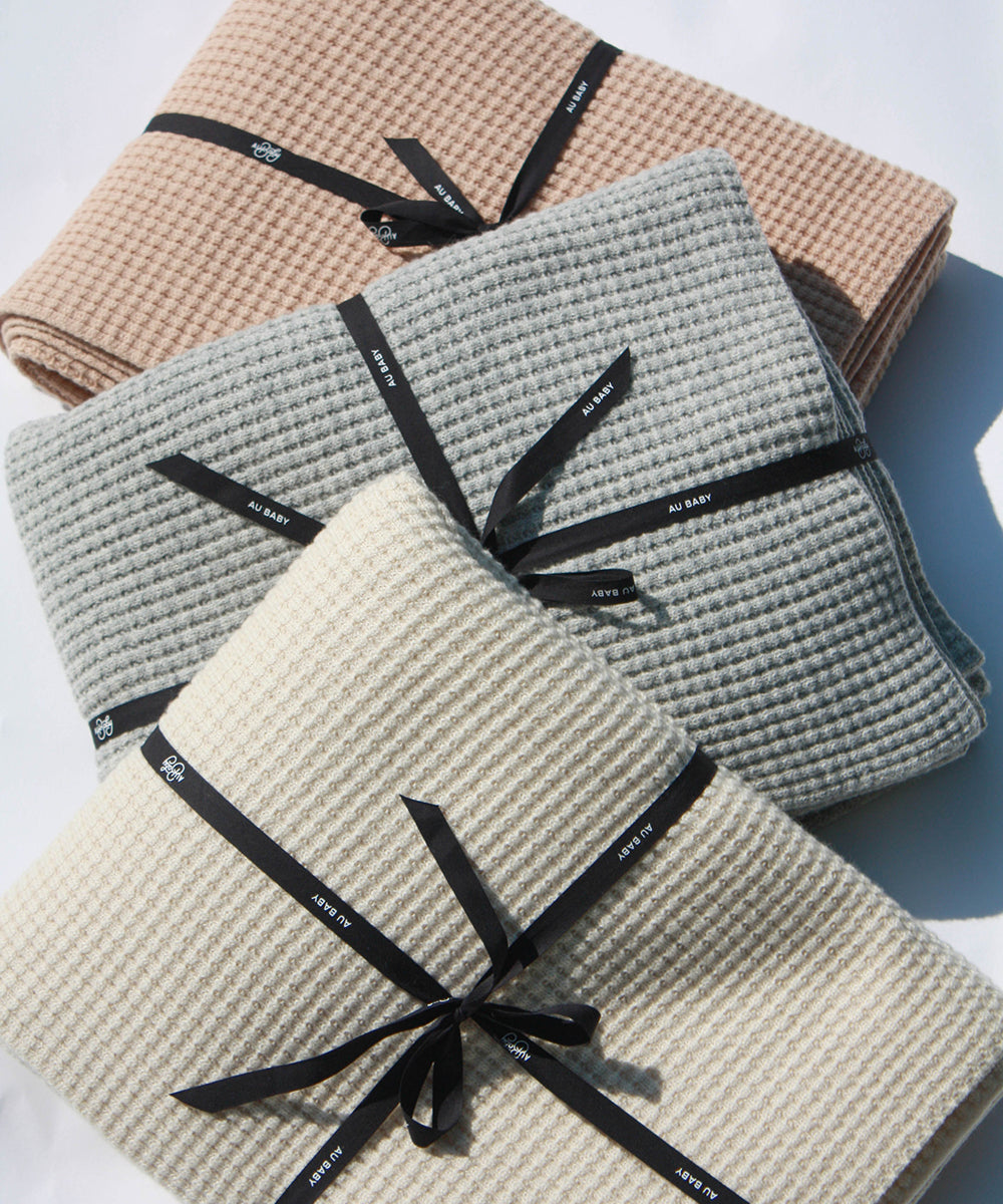 A trio of beautiful AU Baby adult size Popcorn throw blankets folded and tied up with black branded ribbon.