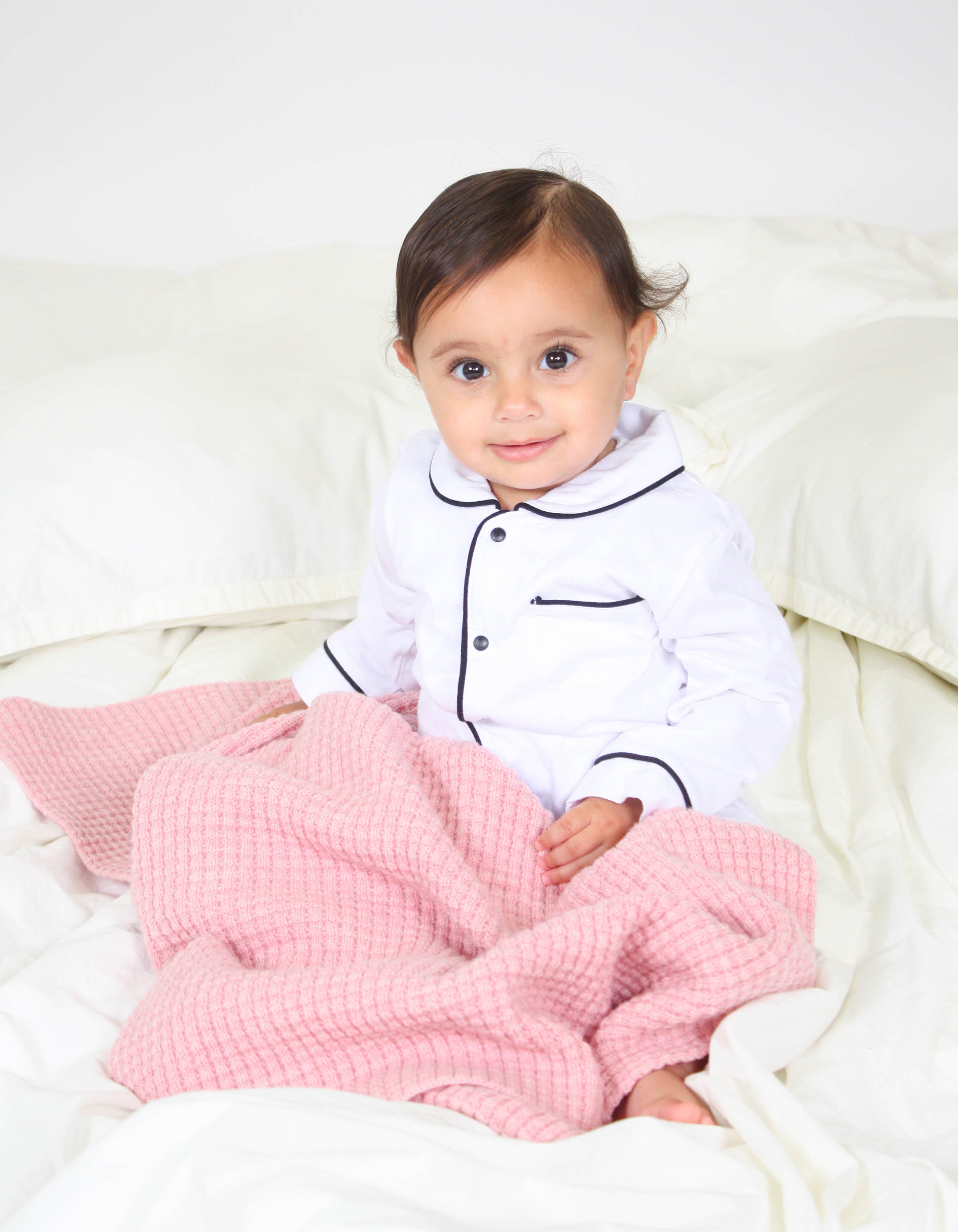 Little girl sitting with AU Baby plant dyed merino Popcorn blanket in Pink Quartz.