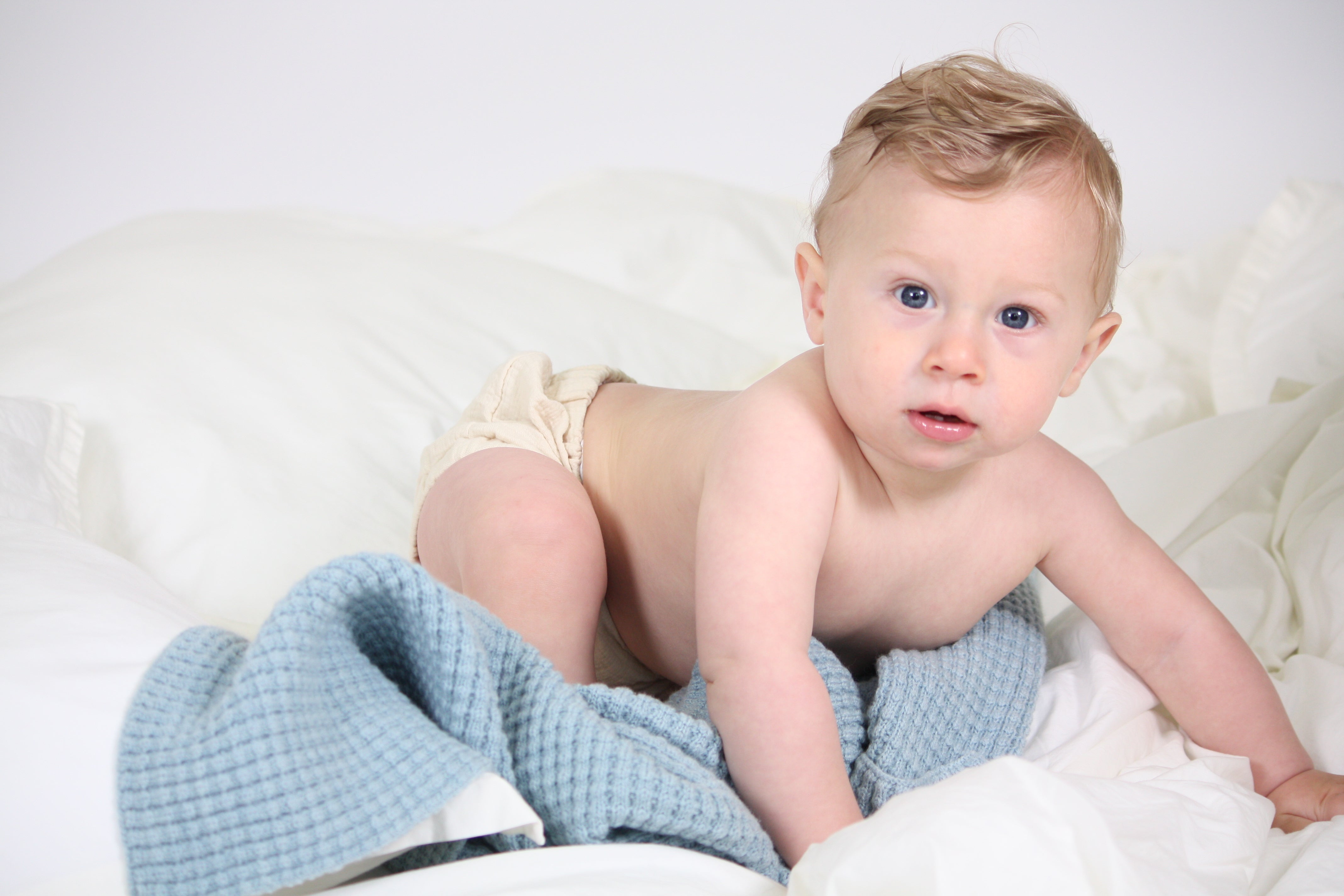 Baby boy relaxing with AU Baby plant dyed merino Popcorn blanket in Blue Sky.