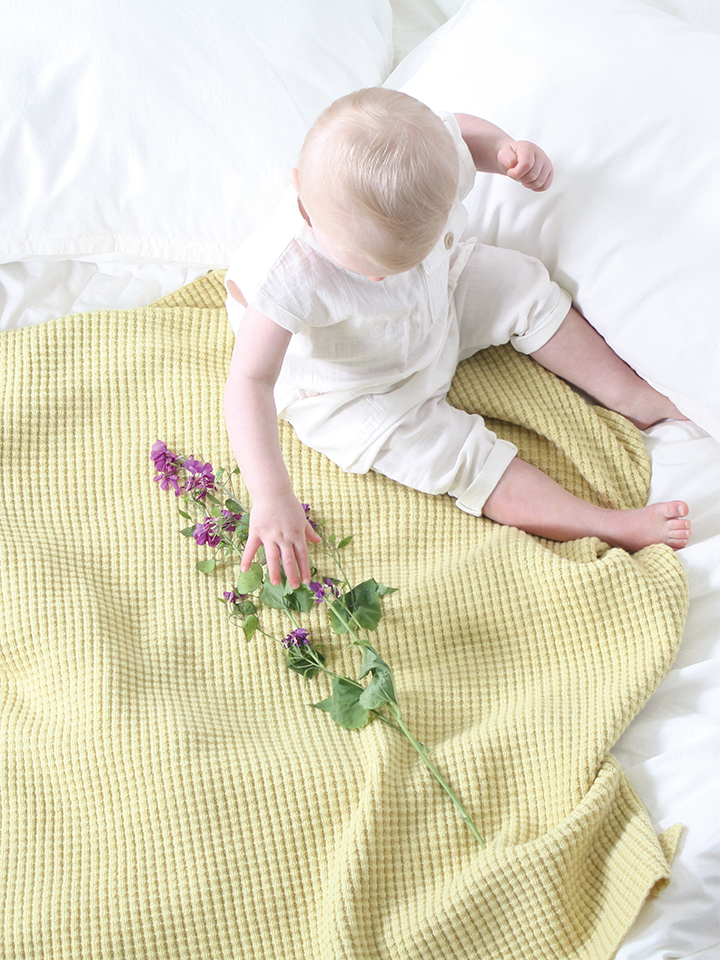 Baby girl sitting on AU Baby plant dyed merino Popcorn blanket in Citron.