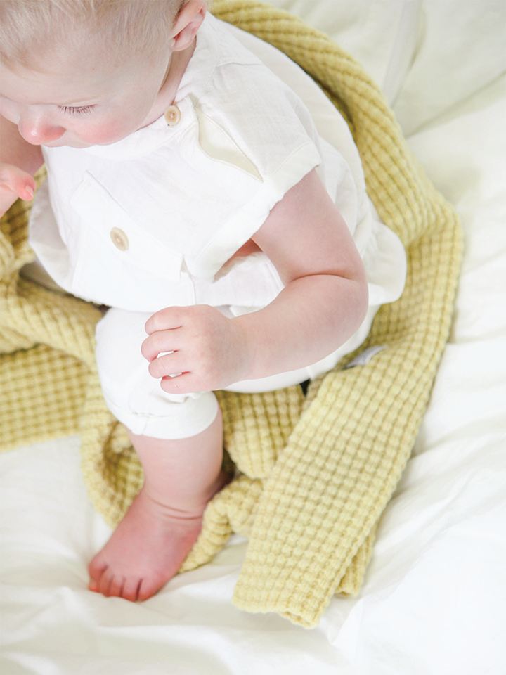 Baby girl sitting on AU Baby plant dyed merino Popcorn blanket in Citron.