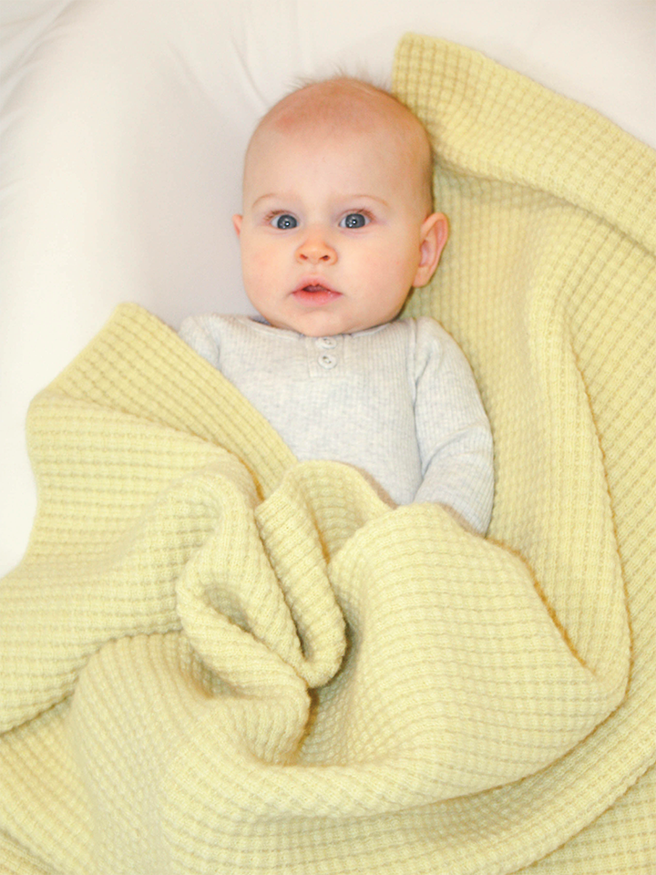 Baby girl snuggling in AU Baby plant dyed merino Popcorn blanket in Citron.